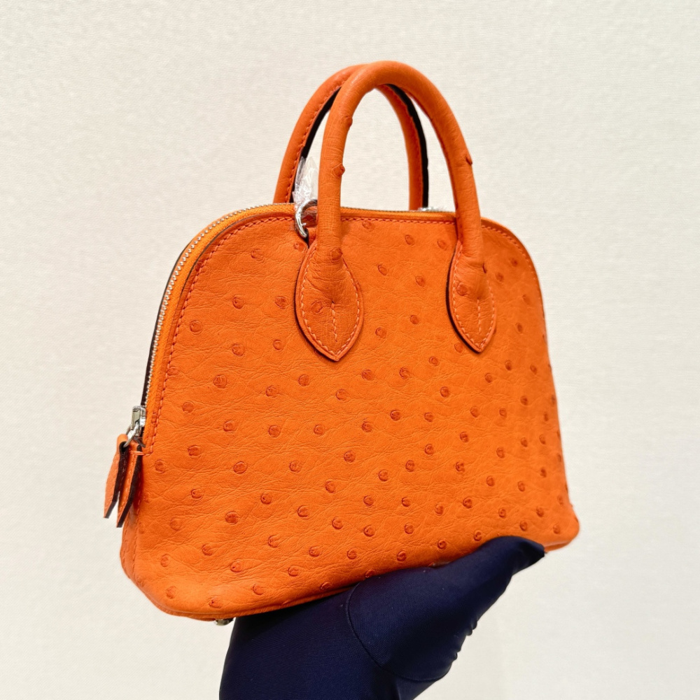 The Hermès Mini Bolide handbag in ostrich leather—featuring the classic Hermès Orange paired with silver hardware—is a highly recognizable and vibrant piece within the brand's exotic skins collection.