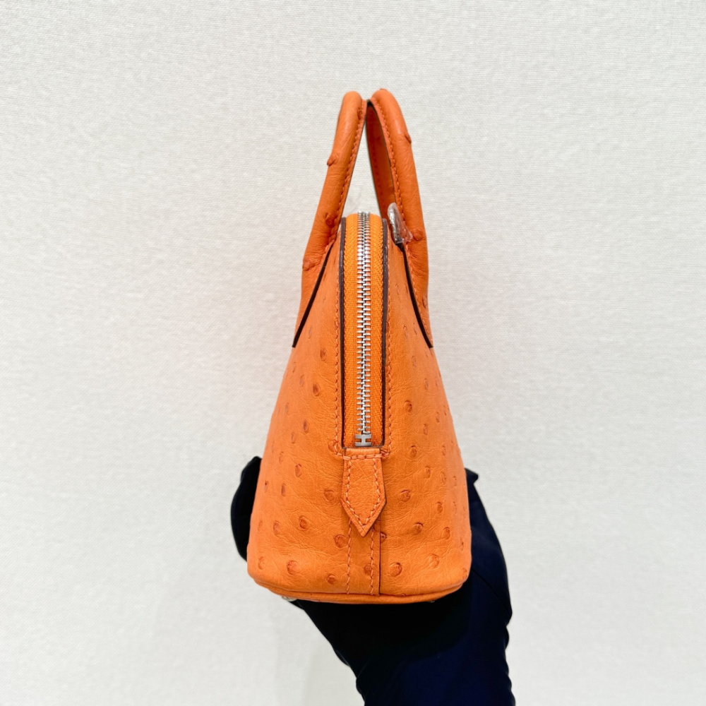 The Hermès Mini Bolide handbag in ostrich leather—featuring the classic Hermès Orange paired with silver hardware—is a highly recognizable and vibrant piece within the brand's exotic skins collection.