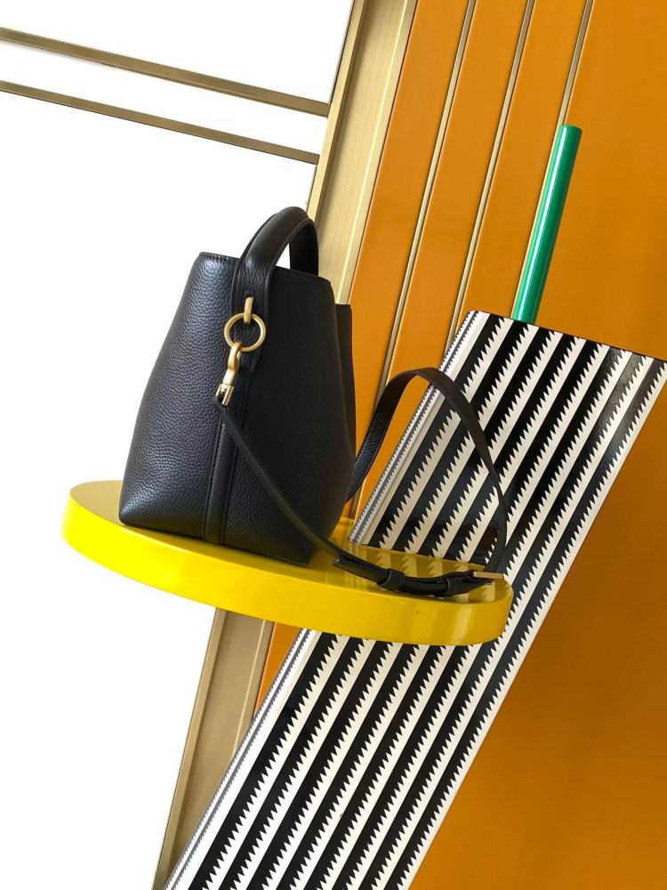 This is a small bucket bag from Yves Saint Laurent (YSL), crafted in black grained leather with a gold-tone YSL logo hardware. It comes with a detachable strap, suitable for both hand-held and crossbody wear.