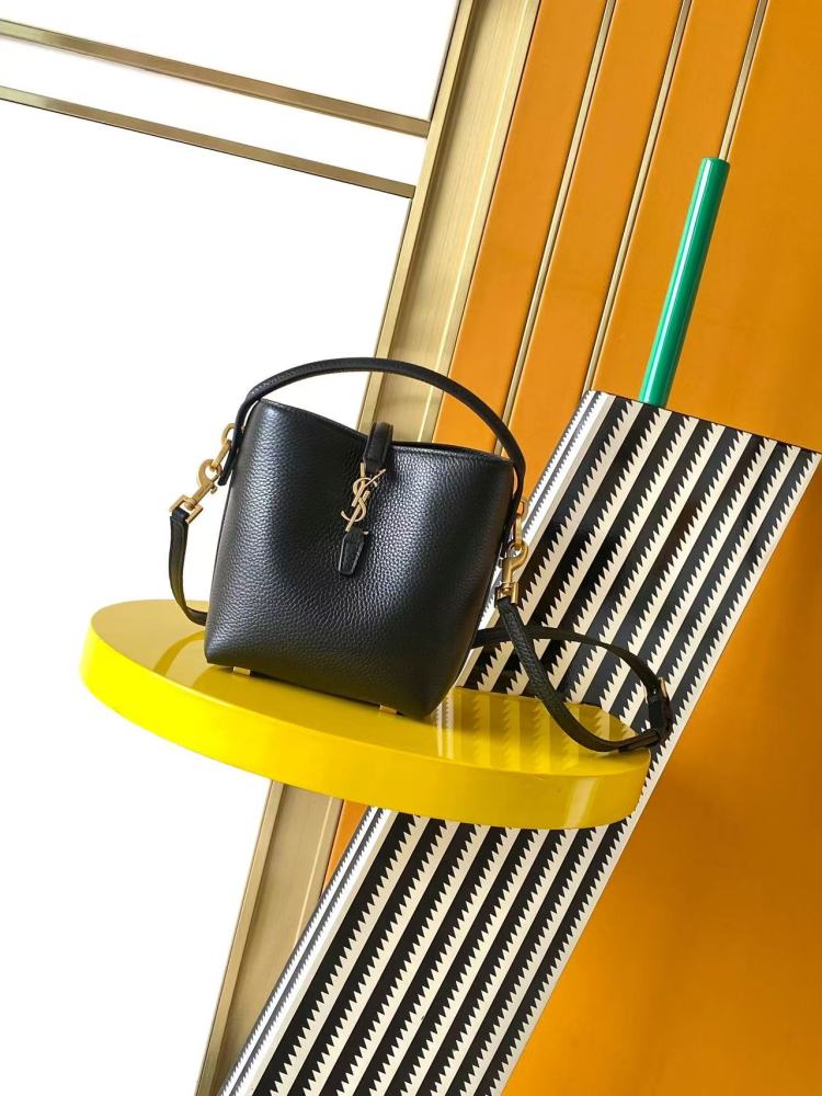 This is a bucket bag from Yves Saint Laurent (YSL), crafted in black grained leather. The front of the bag is adorned with a prominent gold-tone YSL logo hardware. It comes with a detachable short top handle and a long crossbody strap, allowing for multip