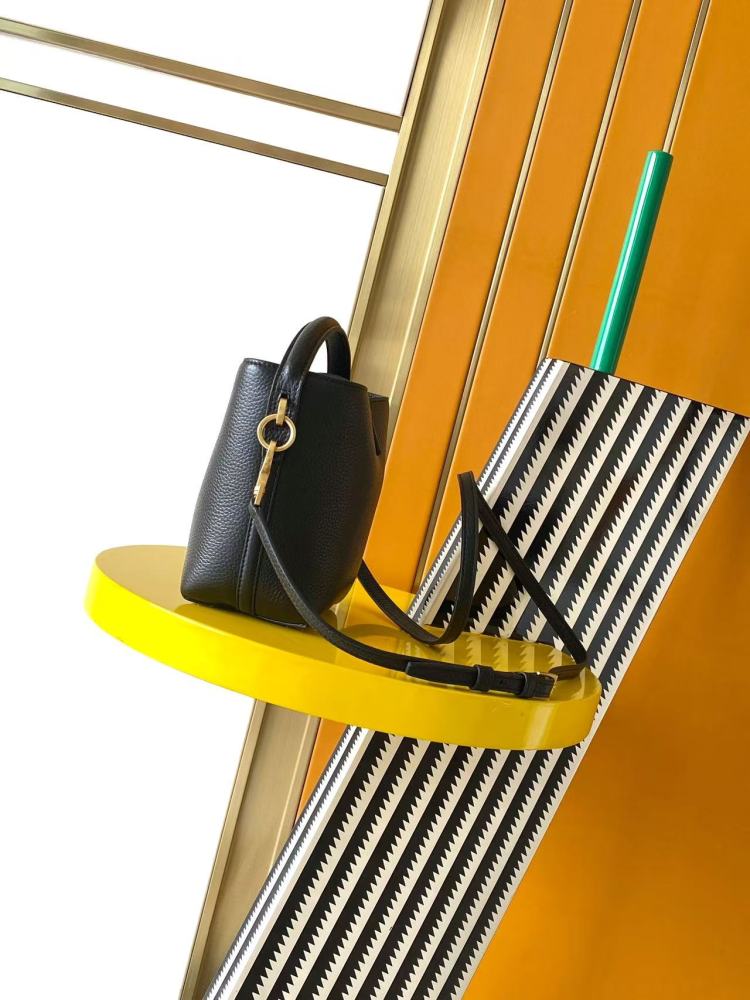 This is a bucket bag from Yves Saint Laurent (YSL), crafted in black grained leather. The front of the bag is adorned with a prominent gold-tone YSL logo hardware. It comes with a detachable short top handle and a long crossbody strap, allowing for multip