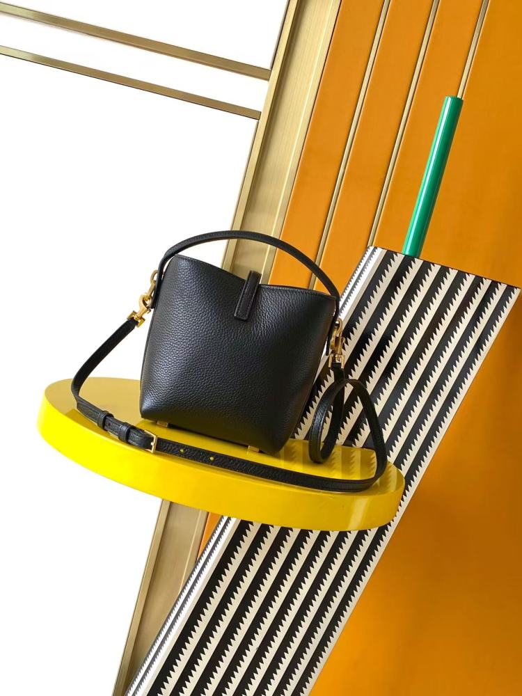 This is a bucket bag from Yves Saint Laurent (YSL), crafted in black grained leather. The front of the bag is adorned with a prominent gold-tone YSL logo hardware. It comes with a detachable short top handle and a long crossbody strap, allowing for multip