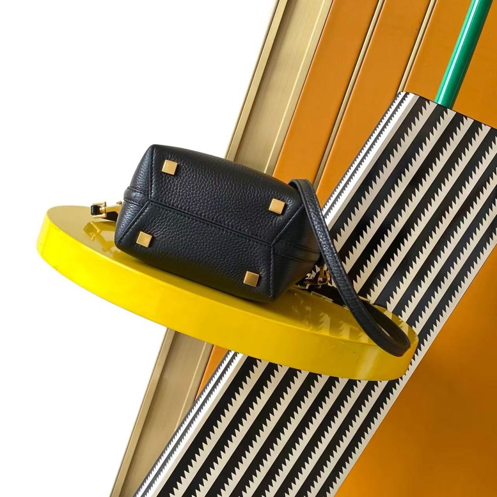 This is a bucket bag from Yves Saint Laurent (YSL), crafted in black grained leather. The front of the bag is adorned with a prominent gold-tone YSL logo hardware. It comes with a detachable short top handle and a long crossbody strap, allowing for multip