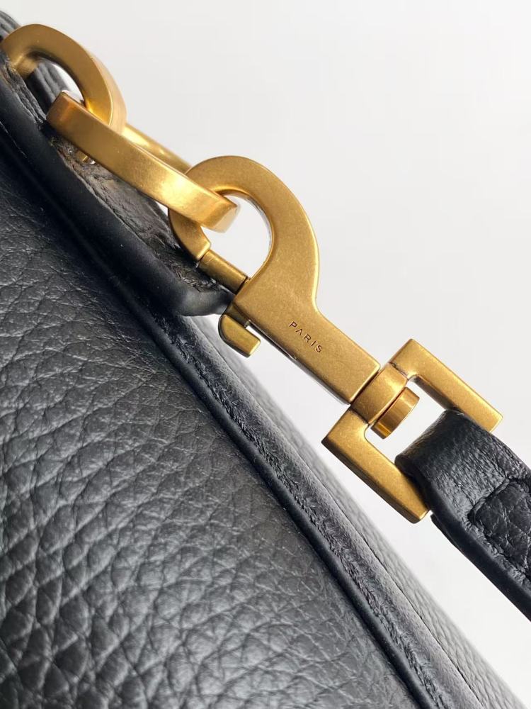 This is a bucket bag from Yves Saint Laurent (YSL), crafted in black grained leather. The front of the bag is adorned with a prominent gold-tone YSL logo hardware. It comes with a detachable short top handle and a long crossbody strap, allowing for multip