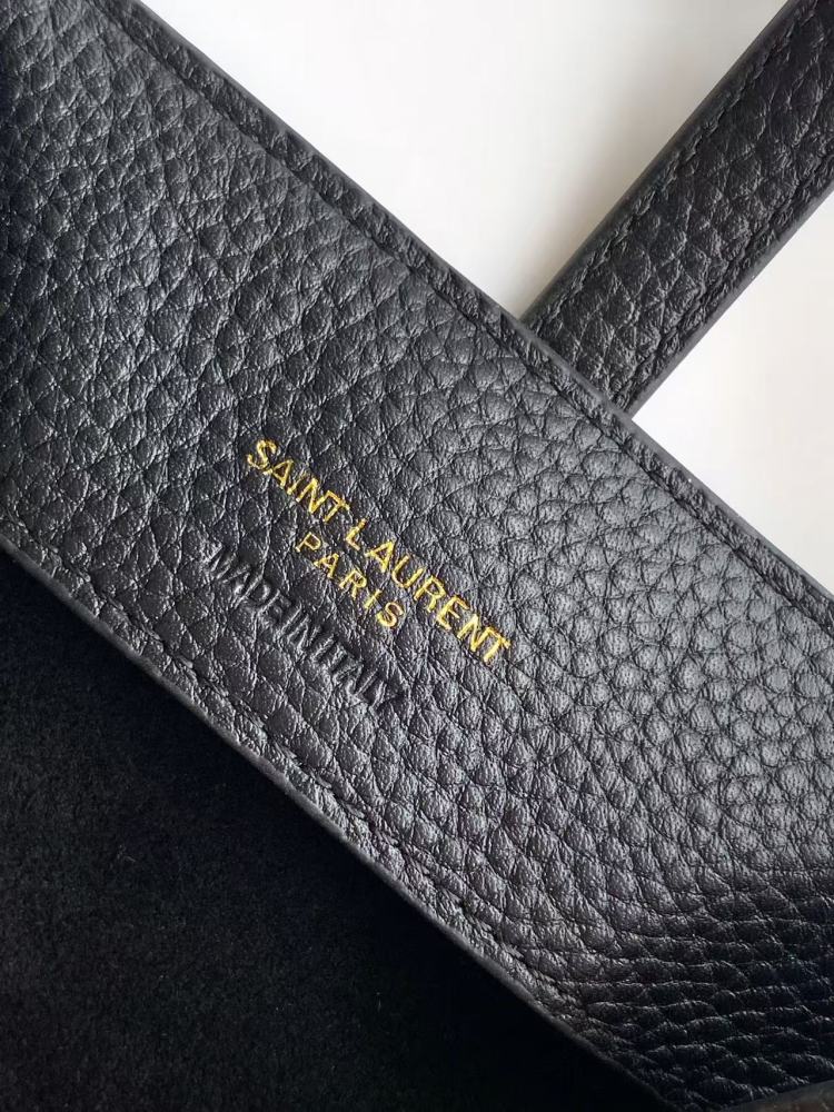 This is a bucket bag from Yves Saint Laurent (YSL), crafted in black grained leather. The front of the bag is adorned with a prominent gold-tone YSL logo hardware. It comes with a detachable short top handle and a long crossbody strap, allowing for multip
