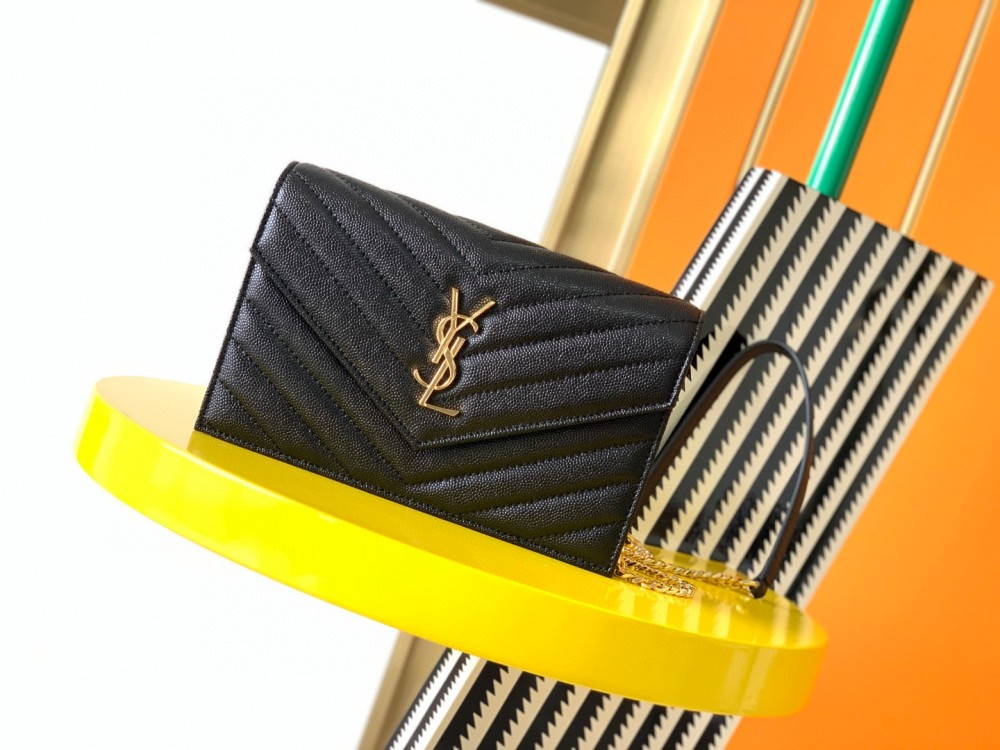 This is the YSL Cassandre chain wallet, crafted from black grained leather with quilted detailing and a gold-tone metal YSL logo on the front. It can be worn as a shoulder or crossbody bag, combining practicality with brand recognition.