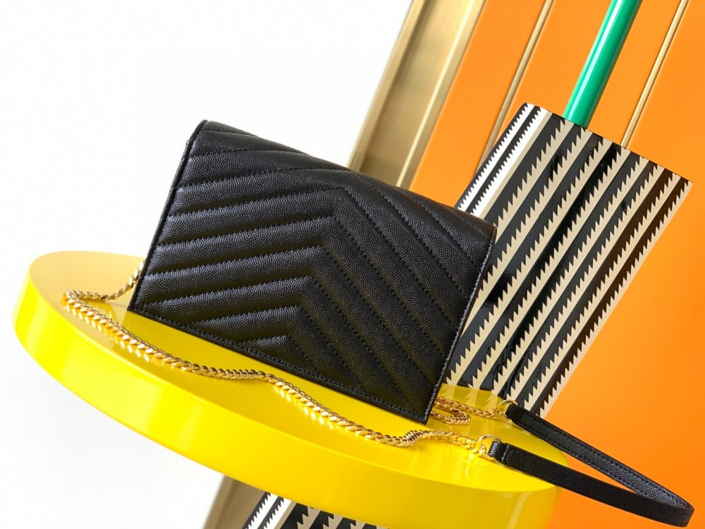 This is the YSL Cassandre chain wallet, crafted from black grained leather with quilted detailing and a gold-tone metal YSL logo on the front. It can be worn as a shoulder or crossbody bag, combining practicality with brand recognition.