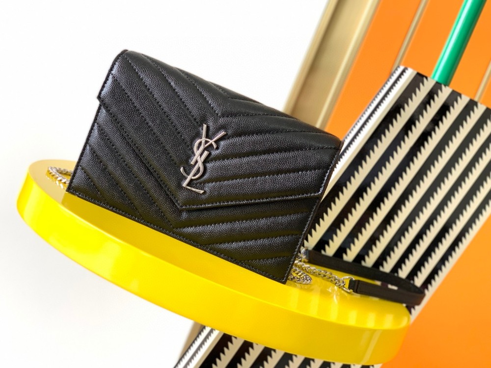 This is the YSL Cassandre chain wallet, crafted from black grained leather with quilted detailing and a silver-tone metal YSL logo on the front. It can be worn as a shoulder or crossbody bag, combining practicality with brand recognition.