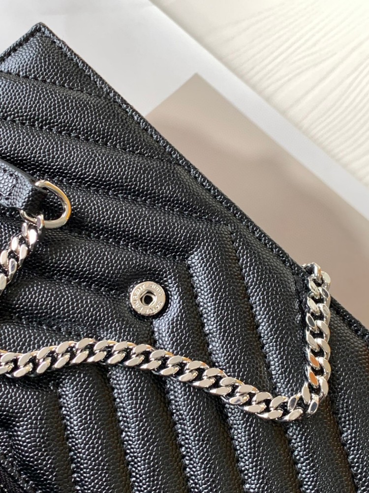 This is the YSL Cassandre chain wallet, crafted from black grained leather with quilted detailing and a silver-tone metal YSL logo on the front. It can be worn as a shoulder or crossbody bag, combining practicality with brand recognition.