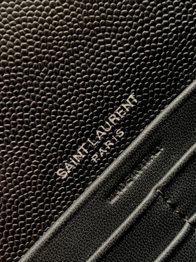 This is the YSL Cassandre chain wallet, crafted from black grained leather with quilted detailing and a silver-tone metal YSL logo on the front. It can be worn as a shoulder or crossbody bag, combining practicality with brand recognition.