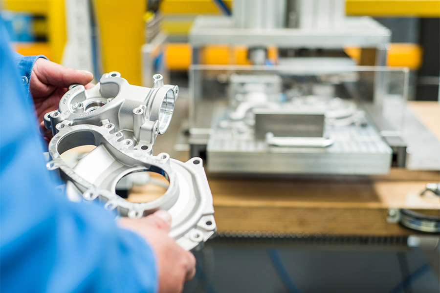 Aluminum die cast housing held in front of a casting machine at the Grace Metal plant