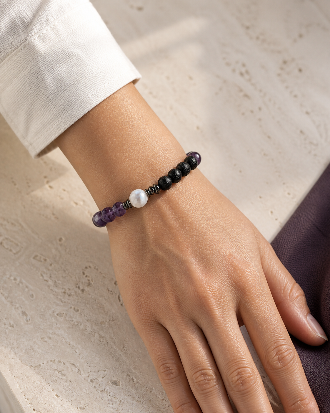 Person wearing a purple and black beaded bracelet with a neutral linen sleeve