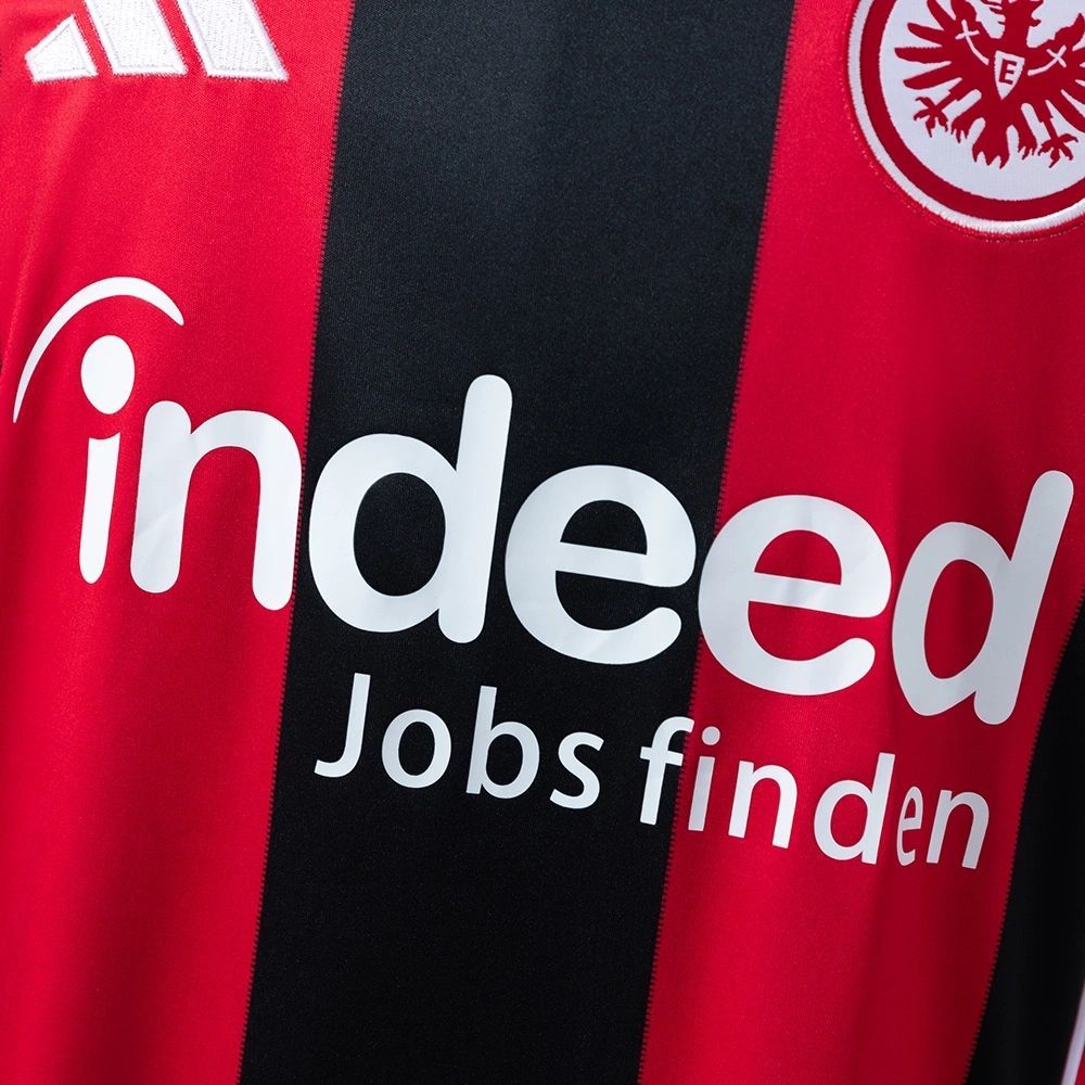 Detail view of the 2025-26 Eintracht Frankfurt home jersey featuring the white ‘Indeed Jobs finden’ sponsor logo across the red and black striped front.