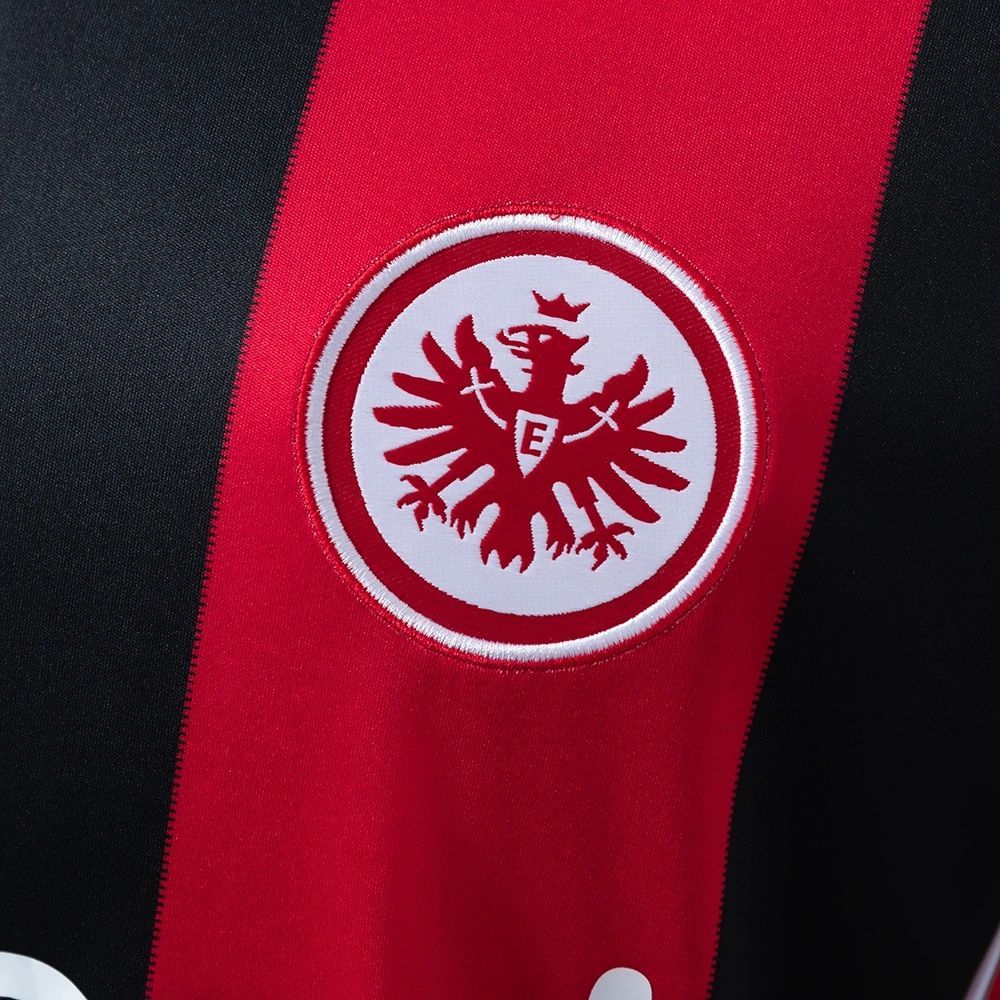 Eintracht Frankfurt 2025-26 home jersey crest close-up featuring the red and white eagle emblem embroidered on the red-and-black stripe design, showcasing the craftsmanship and classic club identity.