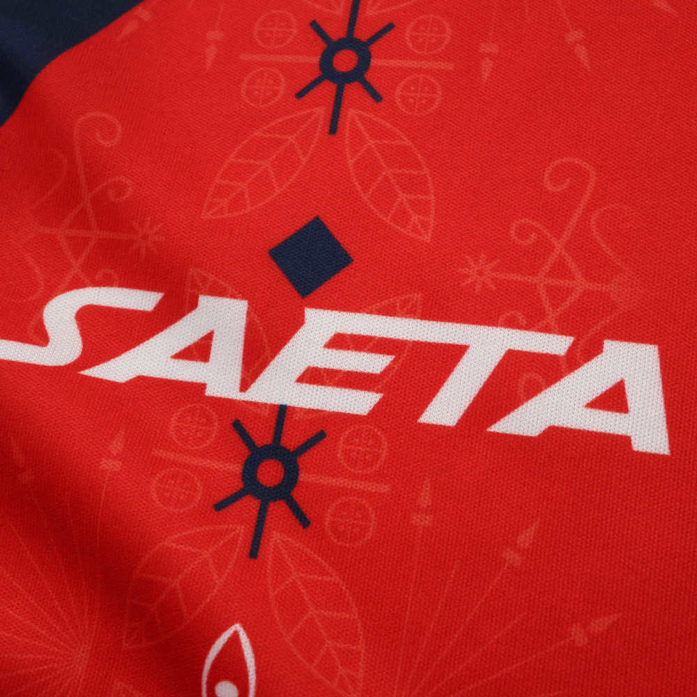 Close-up of the SAETA logo printed on the chest, surrounded by traditional-inspired graphic elements.
