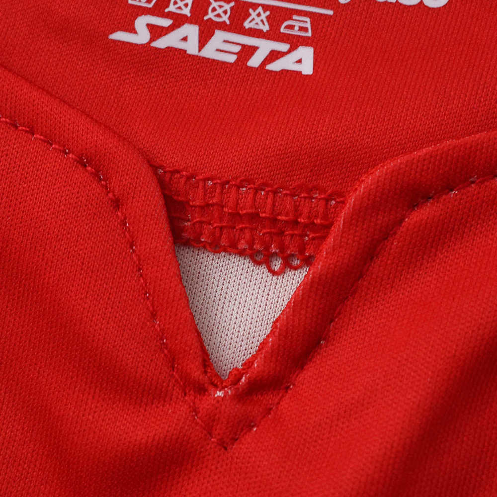 Close-up of the SAETA logo printed on the chest with decorative cultural symbols in the background fabric.