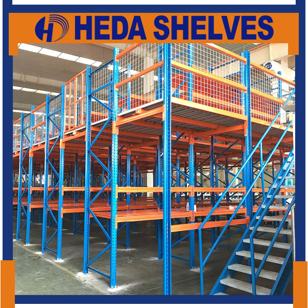Original HEDA No.00293 rack-supported warehouse mezzanine with blue braced steel upright frames, orange storage shelves, orange raised platform, white mesh guardrails and blue steel access staircase