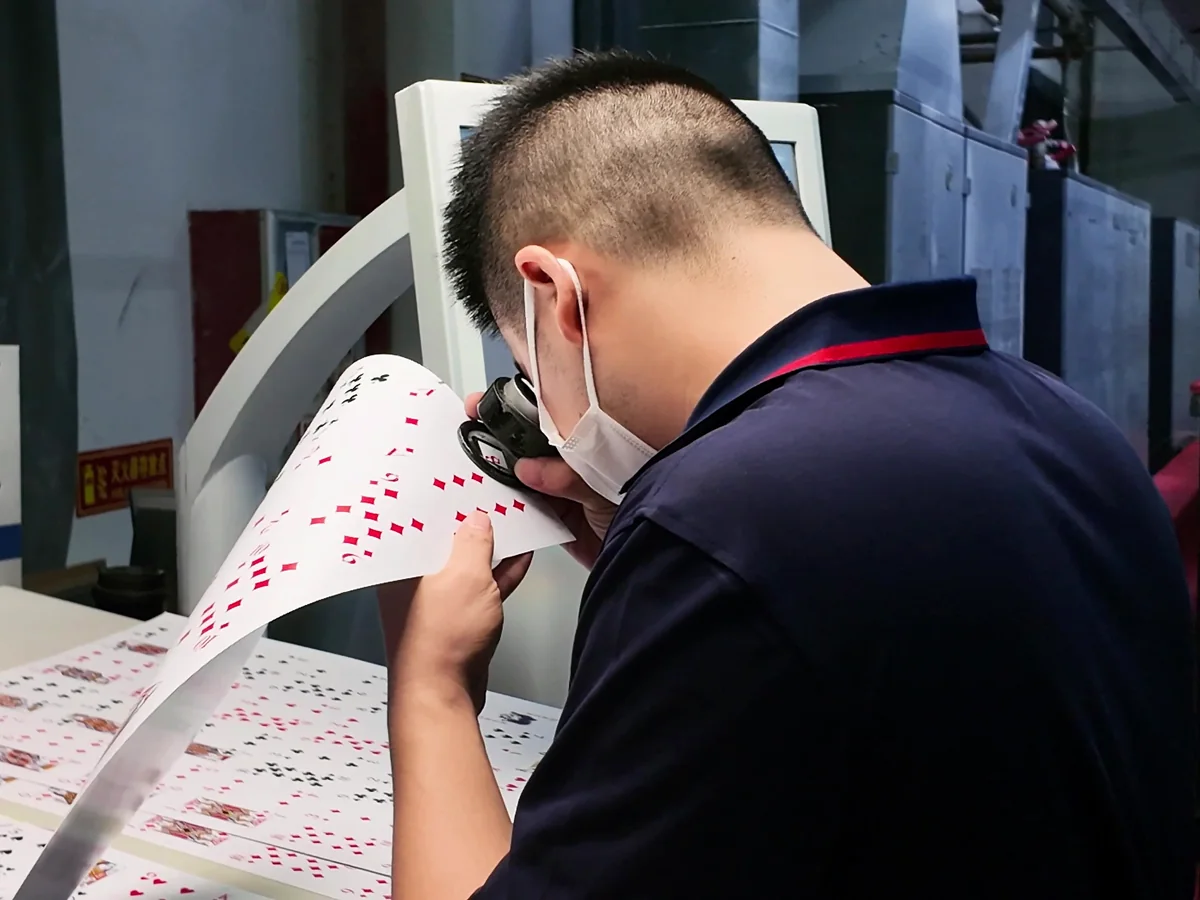 Inspecci&oacute;n del color de una hoja impresa de naipes personalizados con una lupa durante la producci&oacute;n.
