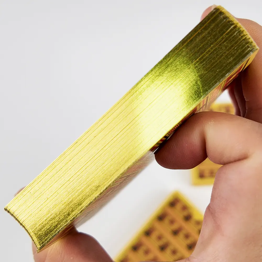 Canto dorado de una baraja personalizada sostenida en la mano, con reversos ornamentales de THRIWA